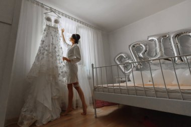 Beyaz etekli güzel bir gelin pencerenin kenarında duruyor, gelinliğine dokunuyor. Düğün için son hazırlıklar. Gelin, damadı bekliyor. Günaydın, gelin..