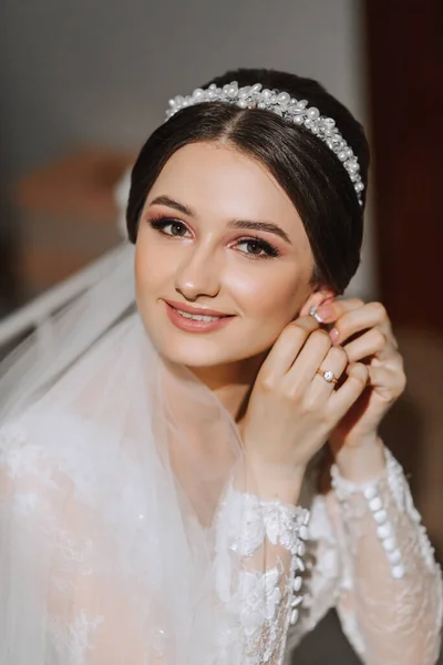 Portrait of a beautiful young bride in a white wedding dress with a tiara on her head. Final preparations for the wedding. The bride is waiting for the groom. Morning, bride.
