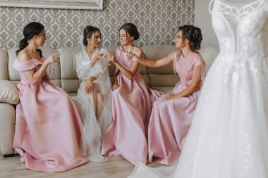 Gelin, aynı pembe elbiseli kız arkadaşlarıyla, sabahları kanepede oturur, ellerinde şampanya kadehleriyle kutlama yapar ve sevinir.