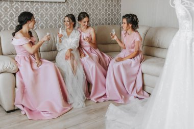 Gelin, aynı pembe elbiseli kız arkadaşlarıyla, sabahları kanepede oturur, ellerinde şampanya kadehleriyle kutlama yapar ve sevinir.