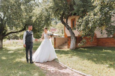 Gelin ve damat düğün töreninden sonra yürür. Bahçede yürüyen genç bir çift. fotoğraf doğada, ormanda, doğada.