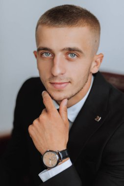 Portre. Beyaz gömlekli ve siyah takım elbiseli bir adam kanepede oturuyor ve poz veriyor. Şık bir saat. Erkek tarzı. Moda. İş dünyası