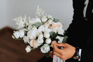 Portre. Beyaz gömlekli, siyah takım elbiseli bir adam koltukta oturuyor, elinde buketle poz veriyor. Şık bir saat. Erkek tarzı. Moda. İş dünyası