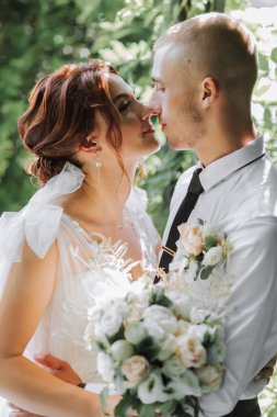 Parktaki gelin ve damadın portresi, gelin ve damat sarılıyor ve şefkatle öpüşüyorlar. Parkta düğün yürüyüşü. Elbisenin uzun treni.