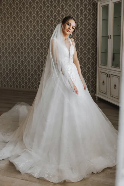The brunette girl is preparing for the wedding. Portrait photo of a bride in a wedding dress with an elegant hairstyle and luxurious makeup, full-length photo