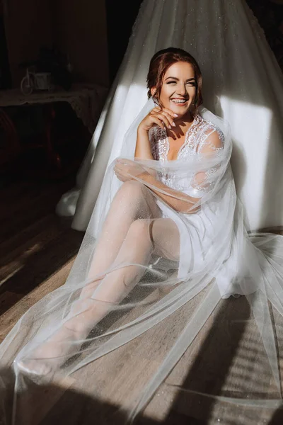 时尚射击 漂亮的女人穿着礼服 迷人的概念 新娘穿着晨衣坐在窗边为摄影师摆姿势 — 图库照片