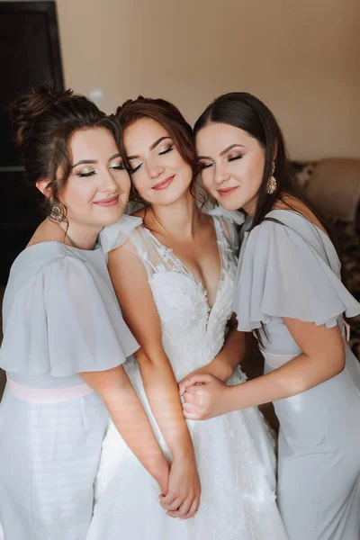 Portrait of the bride with her friends. The bride in a voluminous white dress and her beautiful friends in white evening dresses are posing. Brunettes. Open shoulders. Morning of the bride.