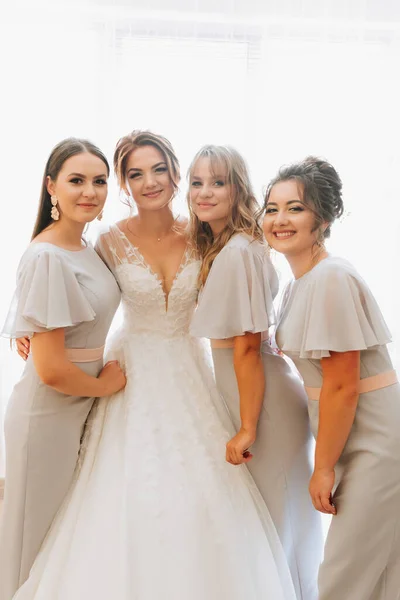 Portrait of the bride with her friends. The bride in a voluminous white dress and her beautiful friends in white evening dresses are posing. Brunettes. Open shoulders. Morning of the bride.