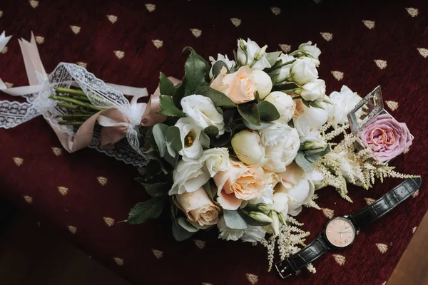 婚礼附件的照片 新郎华丽的花束 金戒指在一个有花的架子上 一只黑色经典手表在勃艮第背景上 — 图库照片