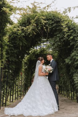 Bir düğün çifti, parktaki yeşil yaprakların arka planına rağmen hayatlarının en güzel gününün tadını çıkarıyor. Doğada aşık gelinlerin portresi