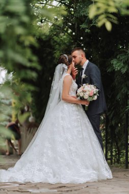 Bir düğün çifti, parktaki yeşil yaprakların arka planına rağmen hayatlarının en güzel gününün tadını çıkarıyor. Doğada aşık gelinlerin portresi