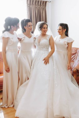 Düğün teması. Beyaz elbiseli gelin arkadaşına sarılıyor ve birlikte poz veriyor. Dört esmer. Düğün hazırlıklarının son dakikaları. Aynı kıyafet.