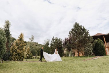 Modaya uygun bir damat ve beyaz elbiseli şirin bir gelin parkta, bahçede, açık havada eğleniyor. Düğün fotoğrafçılığı, geniş açılı fotoğraf