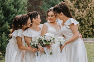 Birbirinin eşi elbiseli bir grup güzel kız gülümsüyor, kutluyor ve birlikte eğleniyorlar doğanın arka planına ve uzun ağaçlara karşı. Kızlar partisi