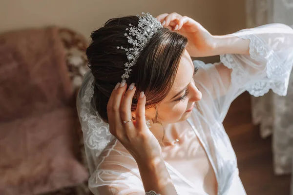 a beautiful bride in a white robe with an open bust and a crown on her head. The bride is preparing for the wedding. bride\'s fees the wedding day of the newlyweds.