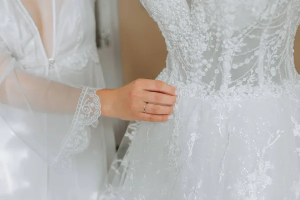 white wedding dress on a mannequin in the room, close-up of the bride's hand on the mannequin. Wedding details, modern wedding dress with long train, long sleeves and open back