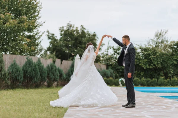 Portrait of the bride and groom. Bride and groom dancing by the pool, holding hands. Wedding walk near the hotel. Long train of the dress
