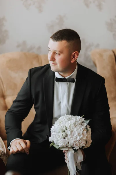 一个身穿白衬衫 身穿黑色西服的男人正坐在沙发上 手里拿着一束鲜花 一个时髦的手表 男人的风格 — 图库照片