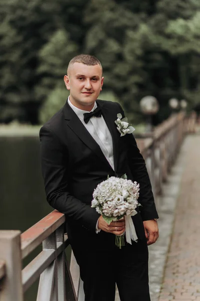 Bröllopsporträtt Man Svart Kostym Står Bro Med Bukett Och Tittar — Stockfoto