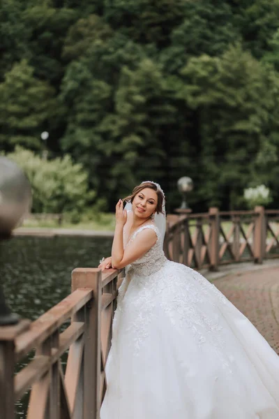 Wedding portrait. The bride in a white dress on the bridge with a flowing veil. Sincere smile. Wind and veil. Diadem.