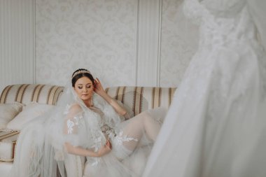 Başında şeffaf bir bornozla düğün saç stili ve taç takmış, kraliyet iç mimarisi olan bir otelde bir yatakta yatan güzel bir kız. Uzun peçe, doğal ışık, portre fotoğrafı.