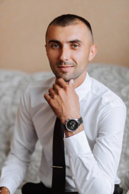 Elinde saat ve kravatla şık bir damat pahalı bir otel odasında sandalyede oturuyor. Damat sabahı. Damat düğün töreninden önce hazırlanıyor..