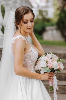 Beyaz gelinlik içinde güzel bir gelinin portresi. Uzun bir tren, modern saç stili ve bahçede yürüyen bir duvak. Düğün konsepti