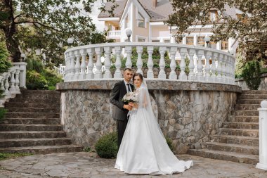 Beyaz elbiseli genç bir gelinin portresi ve merdivenlerde eski bir şehir parkının yakınında sarılan esmer bir damat. Güzel ve romantik bir düğün, mutlu bir çift.