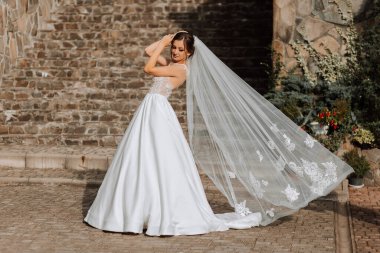 Uzun peçeli, beyaz, şehvetli bir elbiseyle güzel bir gelinin portresi. Güzel saç stili ve profesyonel makyajlı esmer bir kız..