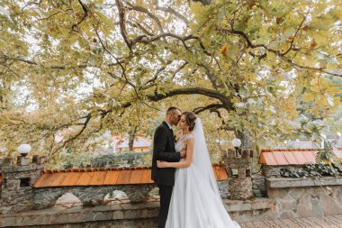 Modaya uygun damat ve beyaz elbiseli yakışıklı esmer gelin profesyonel makyaj ve çiçek buketi ile sarılıyor, parkta, bahçede, ormanda gülüyor. Düğün fotoğrafçılığı