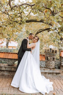 Modaya uygun damat ve beyaz elbiseli yakışıklı esmer gelin profesyonel makyaj ve çiçek buketi ile sarılıyor, parkta, bahçede, ormanda gülüyor. Düğün fotoğrafçılığı