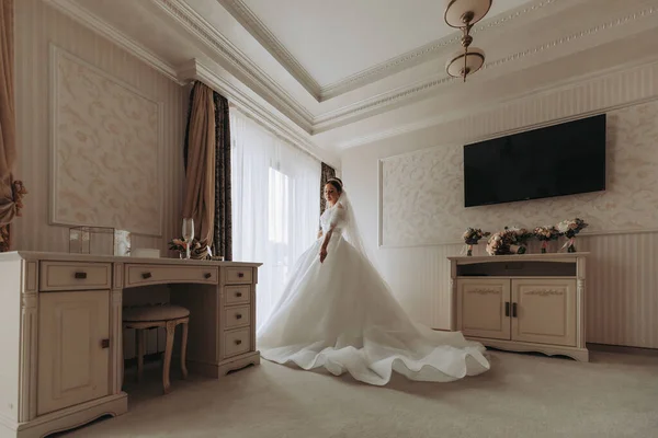結婚式の準備をする 白い豪華なウェディングドレスの美しい若い花嫁 頭にティアラ ロイヤルホテルの部屋の長いベール ベイウィンドウ近くの長い列車と白いドレスのラグジュアリー笑顔モデル — ストック写真