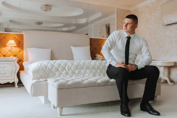 A stylish groom is preparing for the wedding ceremony. Groom\'s morning. Businessman in white shirt in hotel, male hands close-up, groom getting ready in morning before wedding ceremony