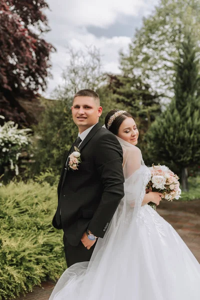 The bride and groom stand back to back. a couple of newlyweds, bride and groom, at a wedding in nature, green forest, kisses, photo portrait. Wedding couple