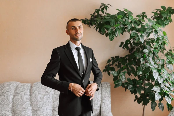 stylish man in a black classic suit with a tie. The groom is preparing for the wedding ceremony