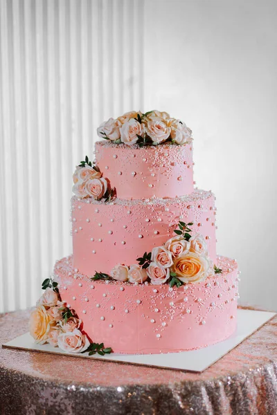 A delicious wedding. Pink three-tiered cake decorated with flowers. Candy bar for a banquet. Celebration concept. Fashionable desserts. Table with sweets, candies. Fruits