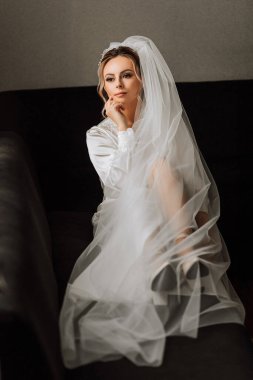 Beyaz saten elbiseli gelin, profesyonel saç ve makyaj, ve uzun bir peçe. Düğünden önceki sabah..