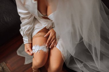 Fransız manikürlü gelin elinde beyaz bir jartiyer tutuyor. Yakın plan fotoğraf. Gelin bir jartiyer takar ve düğün için hazırlanır.