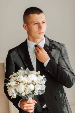Otel odasında bir buket çiçekle şık bir damat. Damat sabahı. Damat düğün töreninden önce hazırlanıyor.