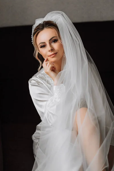 新娘穿着白色缎子长袍 专业的头发和化妆 头戴长长的面纱 婚礼前的早上 — 图库照片