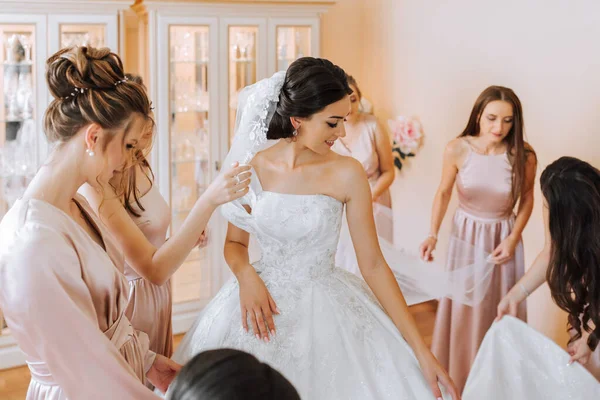 白いドレスで豪華なブルネットの花嫁を助けるシルクドレスにマッチするスタイリッシュな美しい花嫁は 結婚式 朝の準備 ドレスを着る女性の準備をします — ストック写真