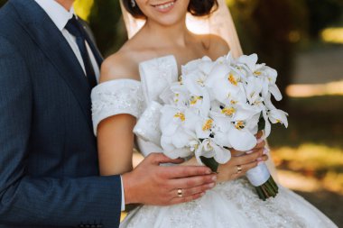 Düğün seremonisinden sonra mutlu gelin ve damat. Uzun peçe. Açık omuzlu şık beyaz elbise. Bir buket orkide. Gün batımında