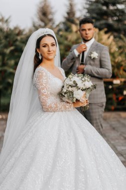 Genç bir düğün çifti yaz otlağında romantik anların tadını çıkarıyor. Başında taç ve duvağı olan bir gelin. Klasik gri takım elbiseli damat.