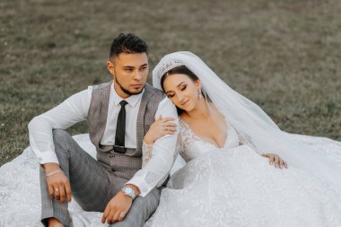 Modaya uygun bir damat ve beyaz elbiseli tatlı esmer gelin parkta, bahçede, dışarıda sarılıp gülüyorlar. Düğün fotoğrafı, gülümseyen yeni evlilerin portresi..