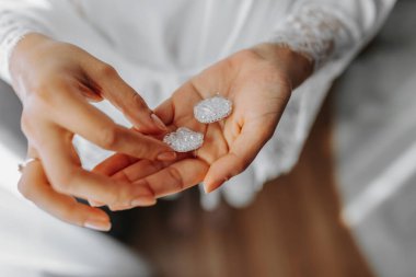 Gelin ellerini tutuyor ve yakın plan değerli taşlarla küpelerini gösteriyor. Gelinin sabahı. Düğün günü..