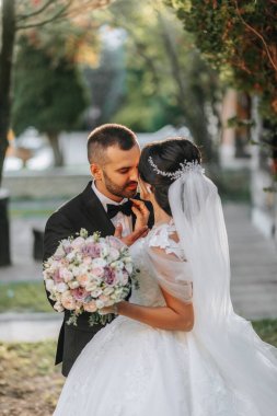 Şık bir gelinlik içinde güzel bir gelin ve damat gün batımında parkta sarılıyor. Büyüleyici genç bir gelin inanılmaz derecede mutlu. Mutlu kız düğün gününde