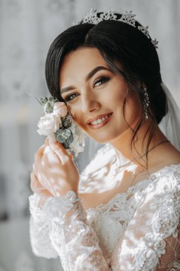 Gelin elinde bir yaka çiçeği tutuyor. Düğün çiçekleri. Lüks bir kadın gününün tadını çıkarıyor. Lüks gelinlik. Profesyonel makyaj.