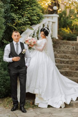 Şık bir gelinlik içinde güzel bir gelin ve zarif bir damat parktaki antik basamaklarda duruyor.