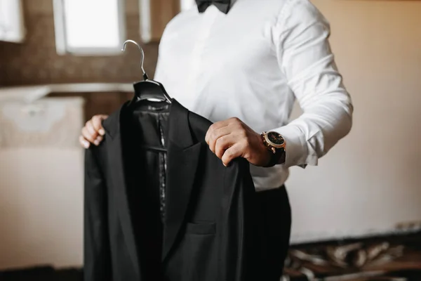 那个人把他的黑色夹克放在手上的衣架上 新郎正在为婚礼做准备 详细的手工特写照片 — 图库照片