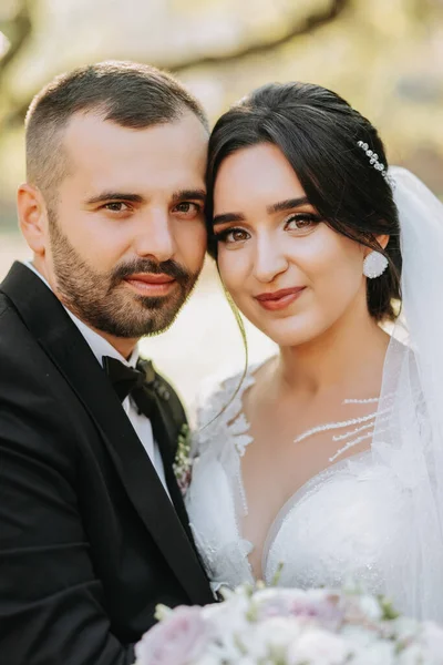 Portrait of a happy newlywed wife and husband hugging outdoors and enjoying a wedding bouquet of white roses. Sincere feelings of two young people. The concept of true love.